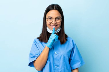 İzole edilmiş mavi arkaplan üzerinde cerrah kadın sessizlik işareti gösteriyor. Parmağını ağzına koy.