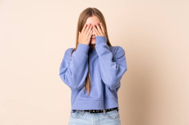 Genç Ukraynalı kız bej arka planda izole edilmiş gözleri elleriyle kapatıyor.