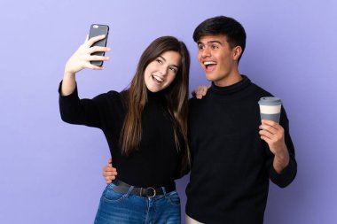 İzole edilmiş mor arka planı olan genç bir çift cep telefonuyla selfie çekiyor.