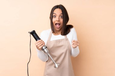 Genç esmer kız el blenderi kullanarak izole bir arkaplanda zaferi kutluyor.