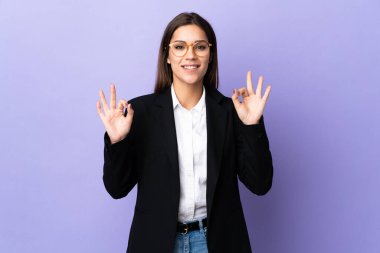 Mor arka planda izole edilmiş bir iş kadını parmaklarıyla tamam işareti gösteriyor.