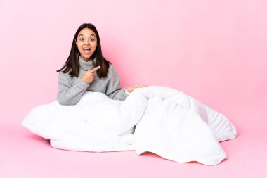 Genç melez kadın pijama giymiş yerde oturuyor şaşırmış ve işaret ediyor.