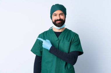 Yeşil üniformalı bir cerrah, izole edilmiş bir zeminde bir ürün sunmak için kenarı işaret ediyor.