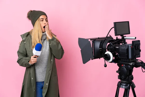 Reporter woman holding a microphone and reporting news over isolated pink background yawning and covering wide open mouth with hand