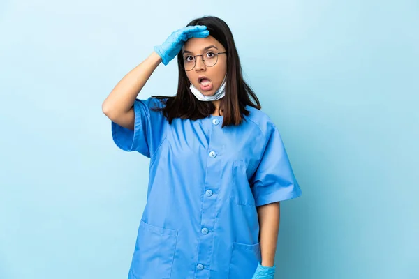 在孤立的蓝色背景上的外科医生女性在向侧面看的时候做出了令人惊讶的动作 — 图库照片