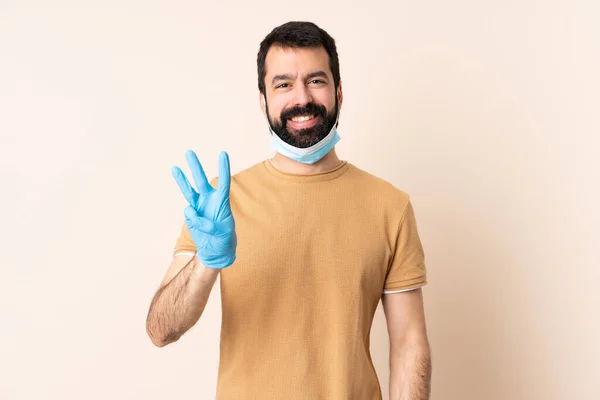 一个白种人 留着胡子 戴着面具和手套 在与世隔绝的背景上 高高兴兴地保护着自己 用手指数着三个人 — 图库照片