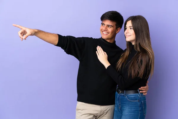 両側に指を指して製品を提示孤立紫色の背景に若いカップル — ストック写真
