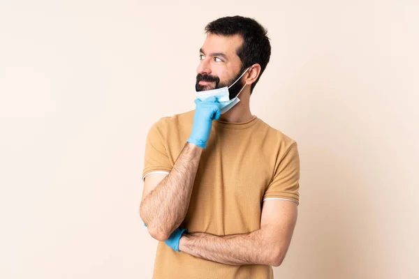 ひげを生やしてコロナウイルスから守る白人男性マスクと手袋で隔離された背景を考えながらアイデアを見上げます — ストック写真