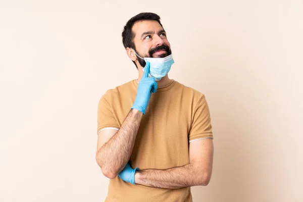 ひげを生やしてコロナウイルスから守る白人男性マスクと手袋で隔離された背景を考えながらアイデアを見上げます — ストック写真