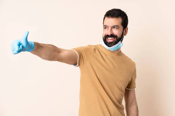 一个白种人 留着胡子 戴着面具和手套 戴在孤立的背景上 竖起大拇指 保护自己不受头皮的侵害 — 图库照片