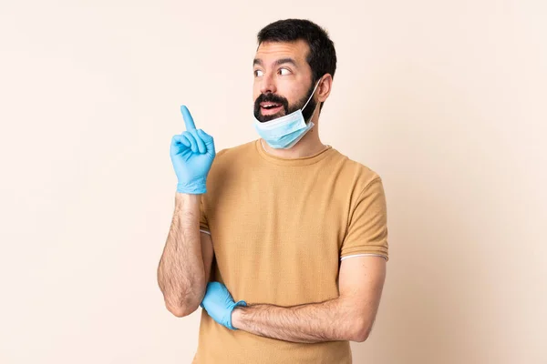 髭を生やしてコロナウイルスから身を守る白人男性マスクと手袋を背景に孤立した考え方で指を指差す — ストック写真