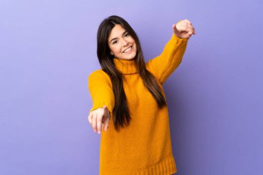 İzole edilmiş mor arka plan üzerinde Brezilyalı genç bir kız mutlu bir ifadeyle önü işaret ediyor