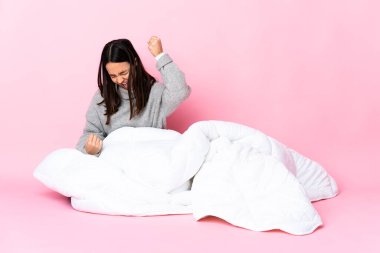 Genç melez kadın pijama giymiş yerde oturmuş zaferi kutluyor.