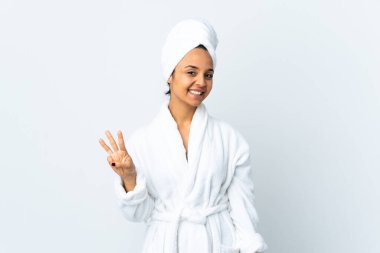 Bornozlu genç kadın izole edilmiş beyaz arka planda mutlu ve parmaklarıyla üçe kadar sayıyor.