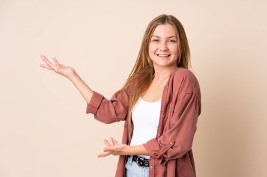 Genç Ukraynalı kız bej arka planda izole edilmiş. Davet etmek için ellerini yana uzatıyor.