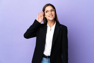 Mor arka planda izole edilmiş bir iş kadını. Kulağına elini sürerek bir şeyler dinliyor.