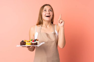 Pastacı Ukraynalı şef pembe arka planda izole edilmiş bir kek tutuyor işaret parmağı ile işaret etmek harika bir fikir.