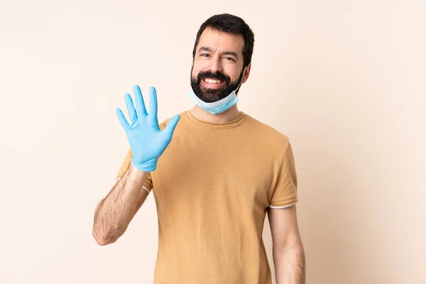 一个白种人 留着胡子 戴着面具 戴着手套 在孤立的背景上保护自己 用手指数着五个人 — 图库照片