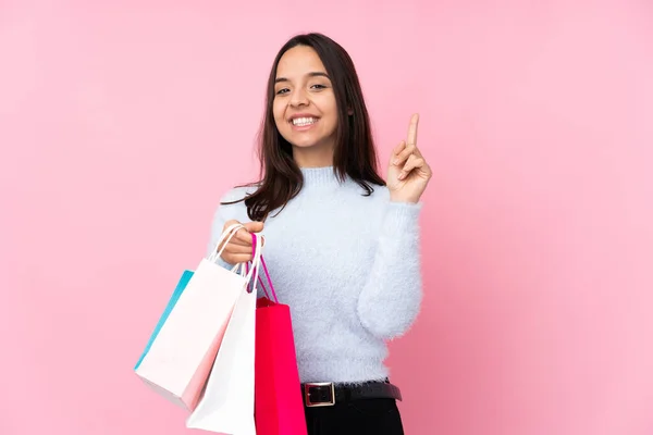 若いです女性とともにショッピングバッグ上の隔離されたピンクの背景ショーと持ち上げる指でベストの印 — ストック写真