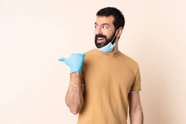 一个白种人 留着胡子 带着面具和手套 带着孤立的背景 保护自己不受头皮的侵害 他指着侧面展示了一种产品 — 图库照片