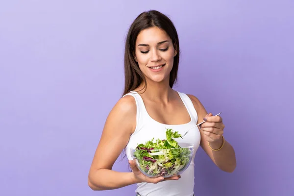 Young caucasian woman with salad isolated on purple background