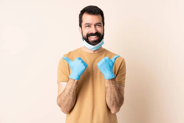 一个白种人 留着胡子 戴着面具 戴着手套 戴在孤立的背景上 带着大拇指 手势和微笑 保护自己不受考拉威斯的伤害 — 图库照片