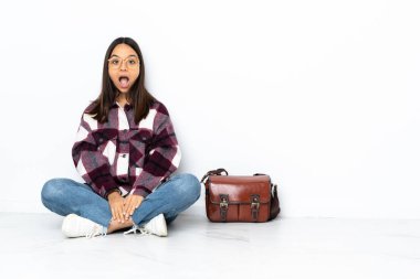 Genç bir bayan öğrenci yerde oturuyor ve yüzünde sürpriz bir ifade var.