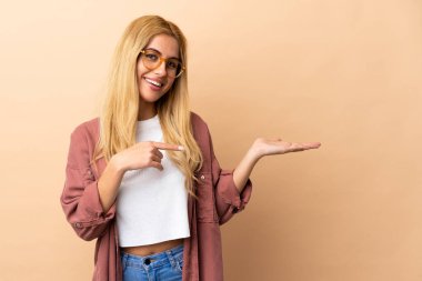 Genç Uruguaylı sarışın kadın, arka planda izole edilmiş. Bir ilan vermek için avucunda hayali bir fotokopi makinesi tutuyor.