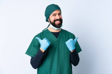 Yeşil üniformalı bir cerrah, izole edilmiş bir geçmişi var. Başparmakları havada ve gülümsüyor.