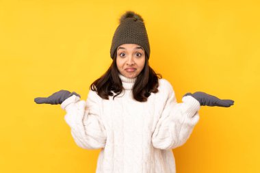 Sarı arka planda, kışlık şapkalı genç kadın ellerini kaldırırken şüpheye düşüyor.