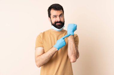 Koronavirüsten sakallı, maskeli ve eldivenli beyaz bir adam geç kalma jestini yapıyor.