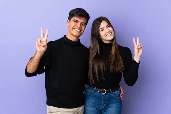 Молода Пара Над Ізольованим Фіолетовим Тлом Посміхається Показує Знак Перемоги — стокове фото