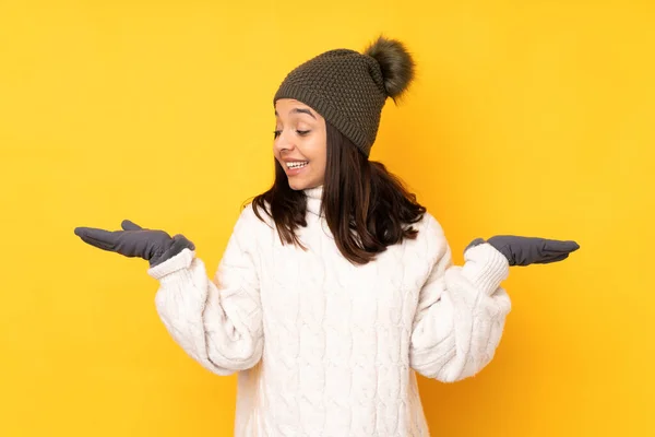 年轻女子 头戴冬帽 身披孤立的黄色背景 双手拿着复制品 — 图库照片