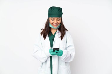 Yeşil üniformalı kadın, beyaz arka planda izole edilmiş. Cep telefonuyla bir mesaj gönderiyor.