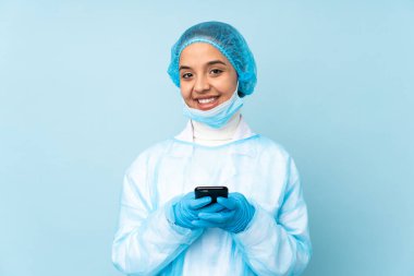 Mavi üniformalı genç bir cerrah cep telefonuyla mesaj yolluyor.