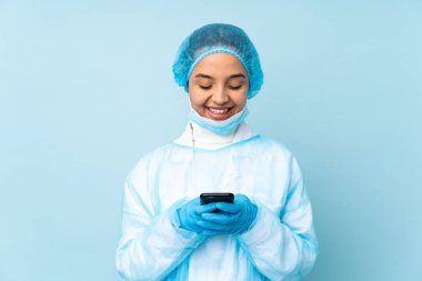 Mavi üniformalı genç bir cerrah cep telefonuyla mesaj yolluyor.