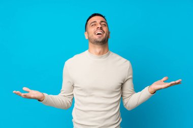 Soyutlanmış mavi arka planı olan genç adam çok gülümsüyor.