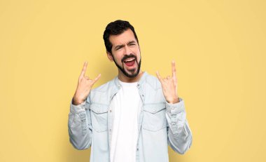 Sakallı yakışıklı adam izole edilmiş sarı arka planda taş hareketi yapıyor.