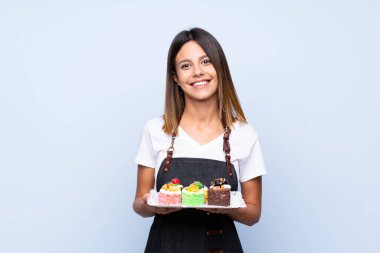 Mini kek tutan, izole edilmiş, mavi arka planı olan genç bir kadın.