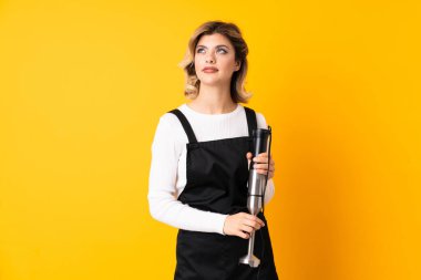 El blenderi kullanan kız sarı arkaplanda izole edilmiş ve yukarı bakarken şüpheleri var