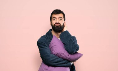 Man with beard in pajamas having doubts over isolated pink background