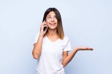 İzole edilmiş mavi arka planı olan genç bir kadın cep telefonuyla sohbet ediyor.