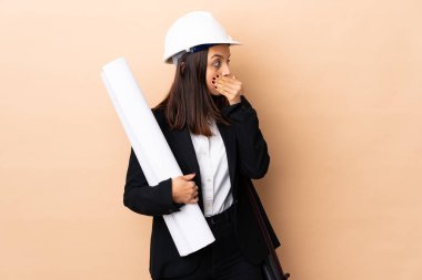 Genç mimar kadının elinde izole edilmiş arka plan planları var. Ağzı kapatıyor ve yan tarafa bakıyor.