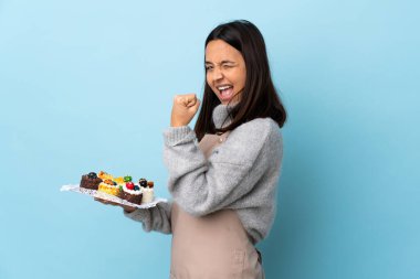 Pasta şefi büyük bir pasta tutuyor ve mavi arka planda zaferi kutluyor..