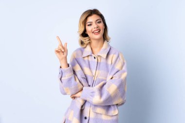 Mavi arka planda izole edilmiş genç Rus kadın en iyinin işareti olarak parmağını kaldırıyor ve gösteriyor.