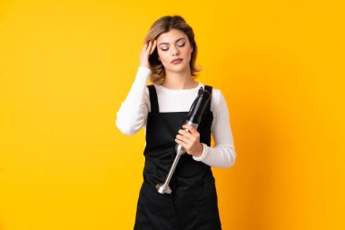 El blenderi kullanan kız sarı arka planda izole edilmiş ve baş ağrısı çekiyor.