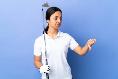 Soyutlanmış renkli arka planda genç golfçü kadın olumsuz ifadeyle baş parmağını aşağı gösteriyor.