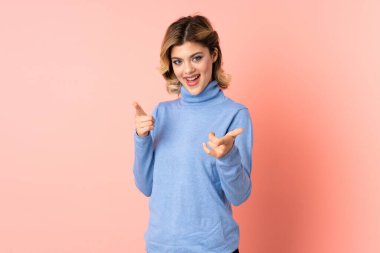 Pembe arka planda izole edilmiş genç Rus kadın şaşırmış ve ön tarafı işaret ediyor.