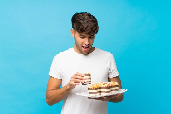 Jonge Knappe Man Geïsoleerde Blauwe Achtergrond Met Mini Taarten Verrast — Stockfoto