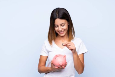 Soyutlanmış mavi arka planı olan genç bir kadın büyük bir kumbara tutuyor.